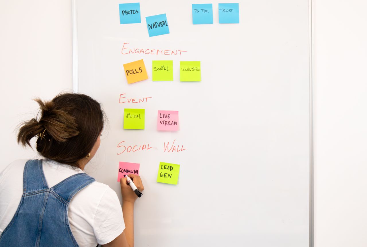 gallery-02 A woman organizing notes on a whiteboard with colorful sticky notes in an office setting.
